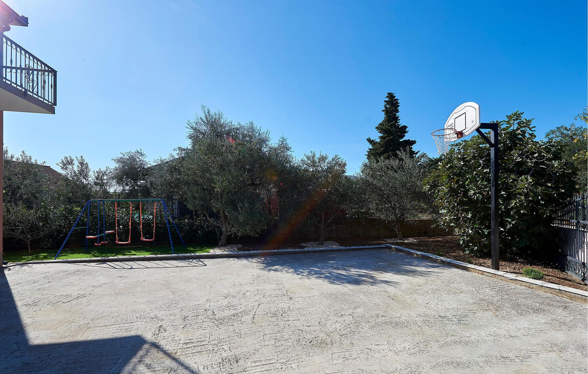 A basketball court with a hoop, swings, and a fence.