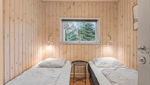 Une petite cabane d’une seule pièce, avec des murs en bois, une fenêtre donnant sur les arbres, deux lits, une petite table et une porte dotée d’un trou de serrure.