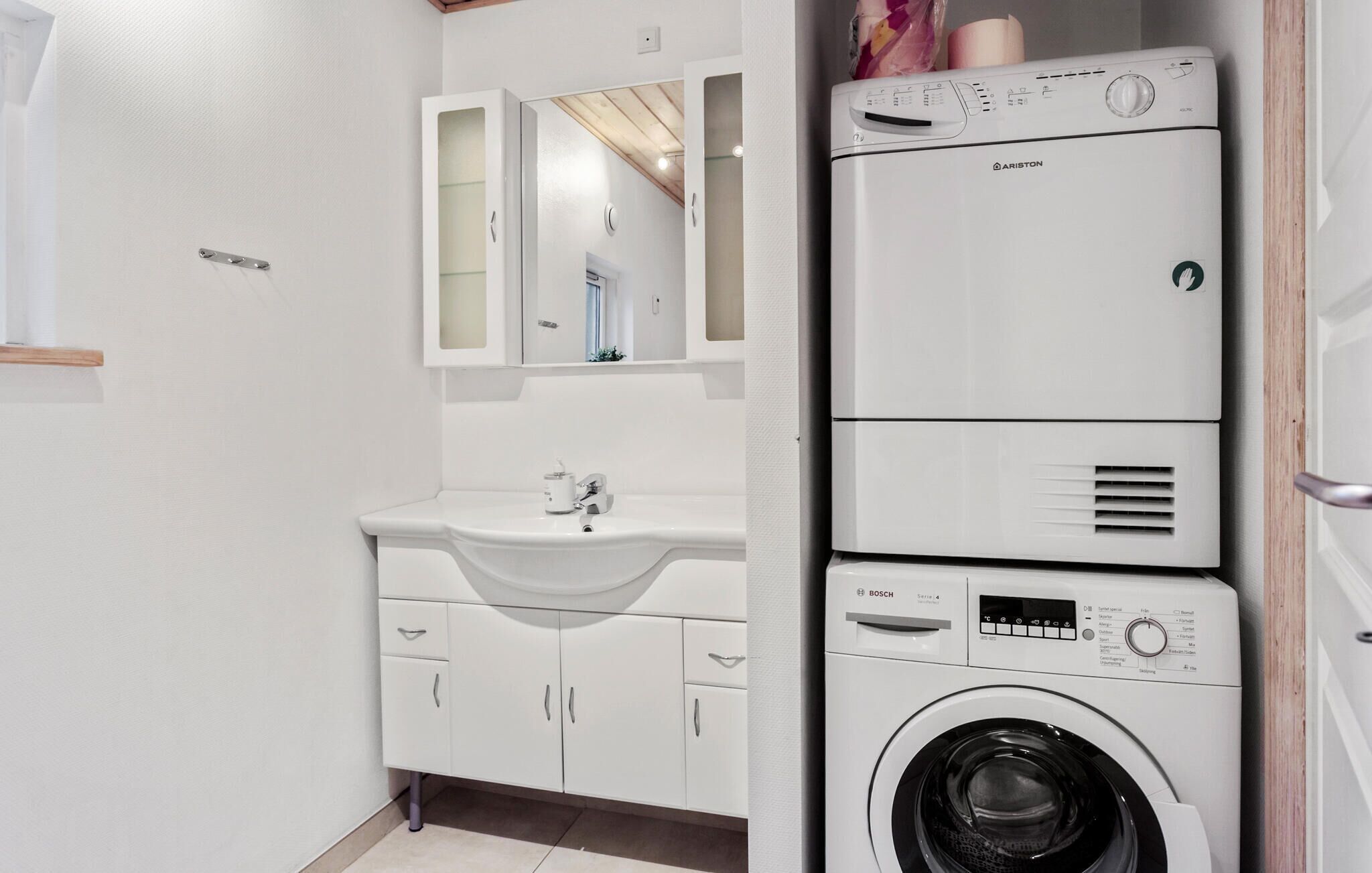 A compact, modern bathroom with a white sink, mirror, and stacked washer and dryer unit.