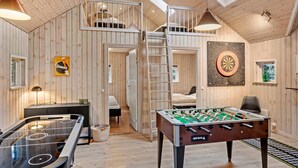 Une pièce chaleureuse avec une table de baby-foot, une chambre en mezzanine avec un lit superposé et un jeu de fléchettes au mur.