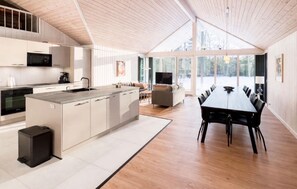 Una cocina moderna con una isla central, una zona de comedor con una mesa larga y un amplio ventanal que ofrece vistas al exterior.