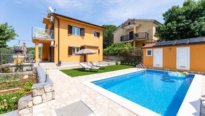 Una moderna casa a due piani con piscina, un patio con poltrone relax e un giardino.