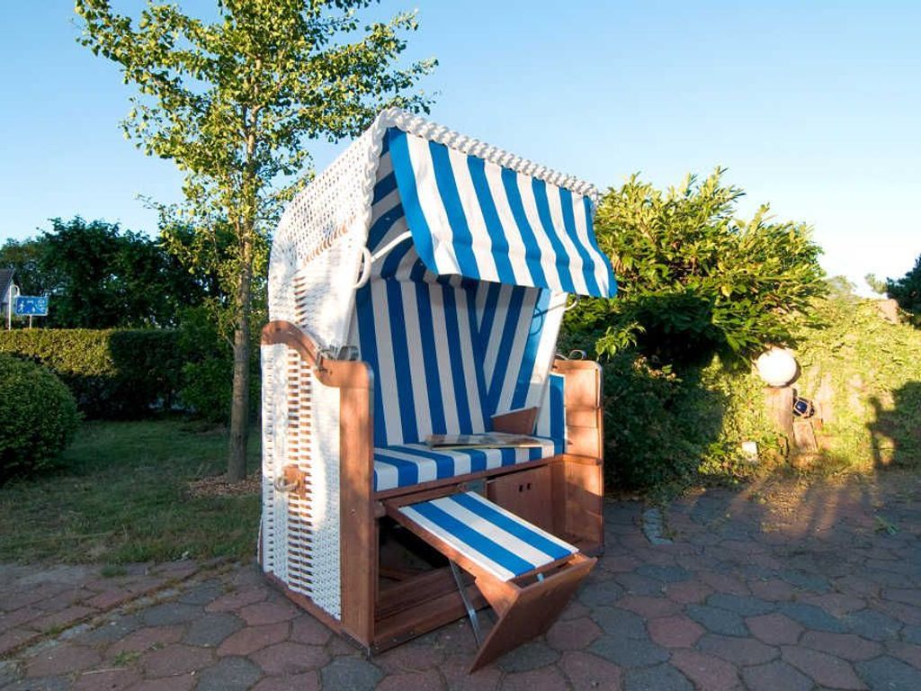 A beach chair with a striped awning, a wooden base, and a white lace cover.