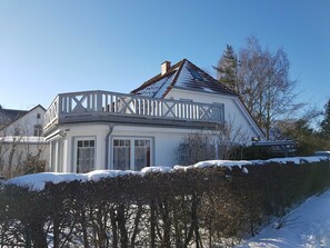A house with a balcony, a snow-covered roof, and a hedge in the foreground. - Nordstrand - Holiday home Ostseesonne (Prerow)