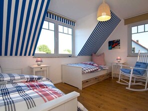 A bedroom with two beds, a rocking chair, a window, and a sloped ceiling. - Nordstrand - Holiday home Ostseesonne (Prerow)