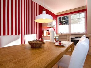Un coin repas avec une table en bois, des chaises blanches, un panier et une suspension blanche.