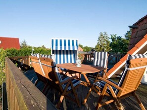 A wooden deck with a table and chairs, a striped umbrella, and a red-roofed building in the background. - Nordstrand - Holiday home Ostseesonne (Prerow)