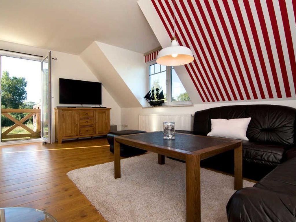 A modern living room with a wooden floor, a black leather sofa, a wooden coffee table, a TV on a wooden cabinet, and a red and white striped ceiling.