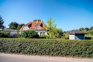 Une maison avec un toit rouge, un balcon et un petit abri de jardin dans le jardin avant.