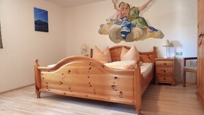 Une chambre à coucher avec un lit en bois, une table de chevet, une commode et une fresque murale.