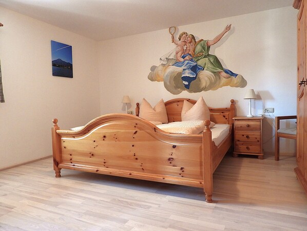 Ein Schlafzimmer mit einem hölzernen Bett, einem Nachttisch, einer Kommode und einer Wandmalerei.