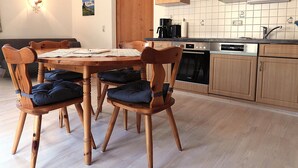 Un coin repas avec une table et des chaises en bois, une cuisine avec des meubles et des appareils électroménagers en bois, et un mur recouvert de carreaux.