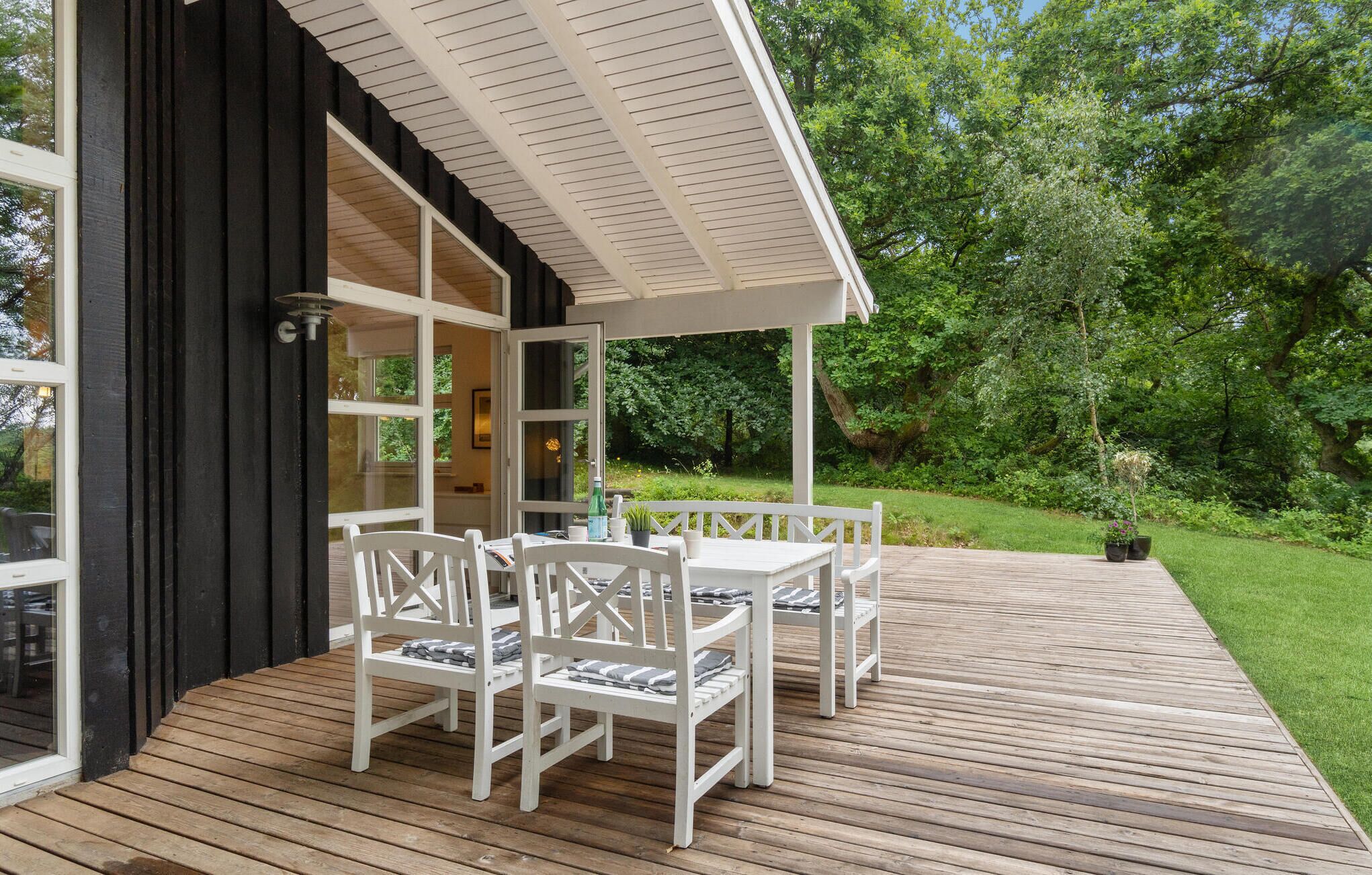 Une terrasse en bois, agrémentée de chaises blanches et d’une table, entourée d’une végétation luxuriante.