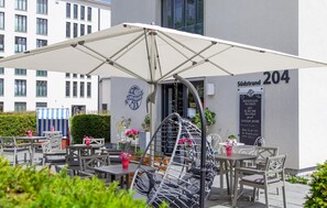 An outdoor café with tables and chairs, a white umbrella, and a sign indicating the address 204 Südstrand. - Beautiful apartment in Binz with WiFi (Prora/Rügen)