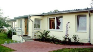 Una casa a un piano con patio in tegole, un piccolo portico e una finestra con tenda.