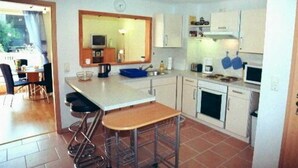 Una cucina compatta con isola centrale, sgabelli da bar ed elettrodomestici essenziali.