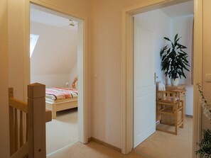 A bedroom with a bed, a wooden chair, a potted plant, and a small table.