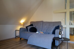 A modern living room with a grey sofa, a small round table, and a bottle of wine. - Himmel-Blick - Vacation Apartment Himmel-Blick (Pünderich)