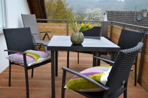 A balcony with a table and chairs, a vase with flowers, and a view of trees and buildings. - Himmel-Blick - Vacation Apartment Himmel-Blick (Pünderich)