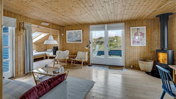 A cozy cabin interior with wooden walls and ceiling, a glass table, a sofa, and a fireplace. - Cozy home in Frøstrup with kitchen (Frøstrup)