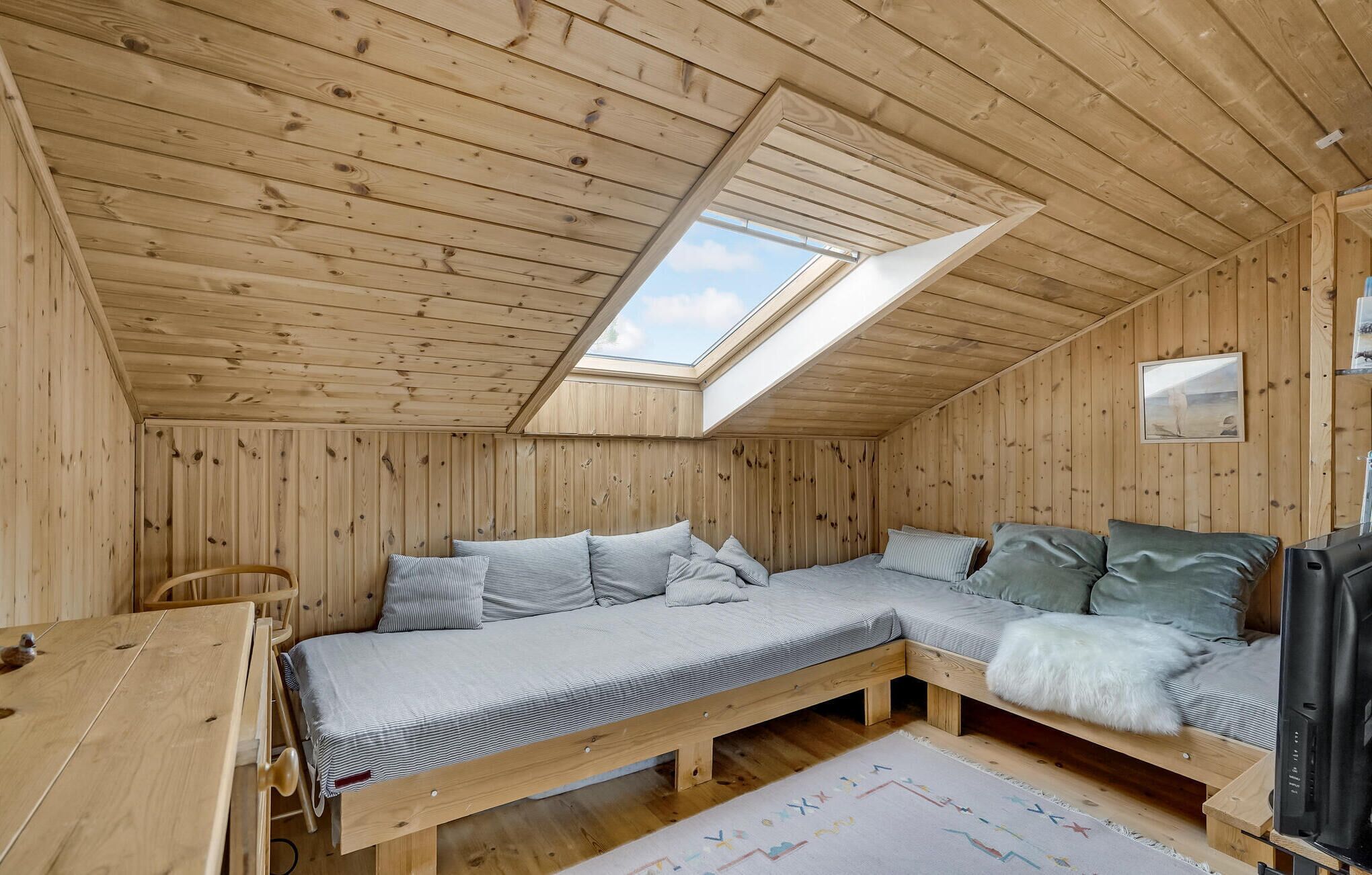 A cozy wooden cabin room with a loft bed, a desk, and a television.