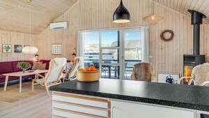A cozy cabin interior with a wooden interior, a large window, a kitchen area, and a fireplace. - Cozy home in Hvide Sande with sauna (Hvide Sande)