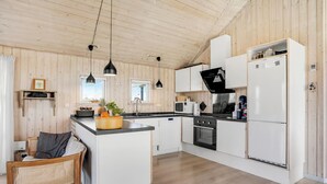 A modern kitchen with wooden paneling, white cabinetry, a central island, and pendant lighting. - Cozy home in Hvide Sande with sauna (Hvide Sande)