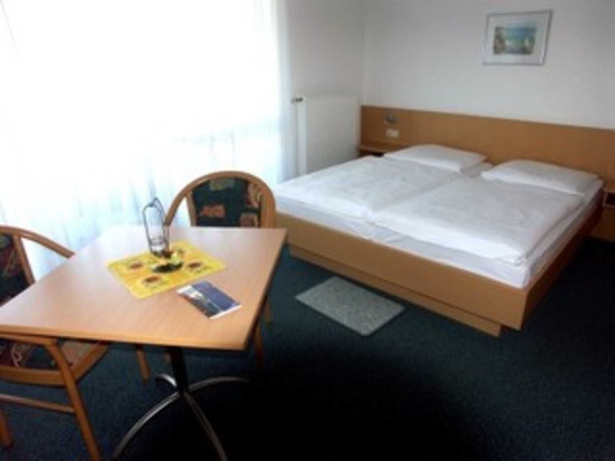A hotel room with a bed, a table with a chair, and a small rug.