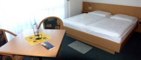 A hotel room with a bed, a table with a chair, and a small rug.
