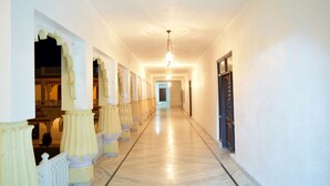 A long, well-lit corridor with ornate columns and a marble floor, leading to a door at the end. - Menal Jungle Safari Resort (Begun)
