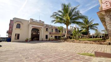 A courtyard with a palm tree, a building with arched windows, and a paved walkway.