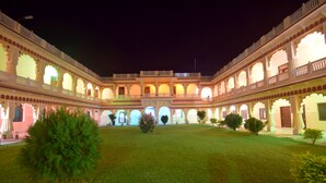 A courtyard with a central open space, surrounded by multiple levels of arched balconies and a well-maintained lawn. - Menal Jungle Safari Resort (Begun)