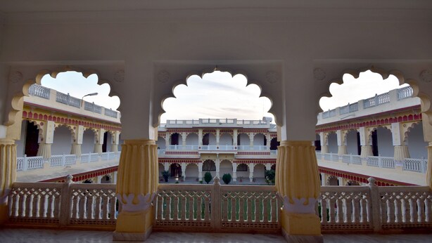 A grand architectural structure with multiple balconies and arches, featuring intricate railings and a marble floor. - Menal Jungle Safari Resort (Begun)