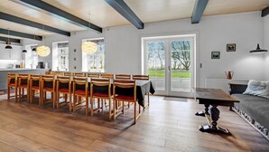 A spacious dining area with wooden chairs and a table, a kitchen in the background, and a large sliding glass door leading to a garden.