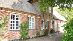 A traditional brick house with a thatched roof, white-framed windows, and a gravel driveway.