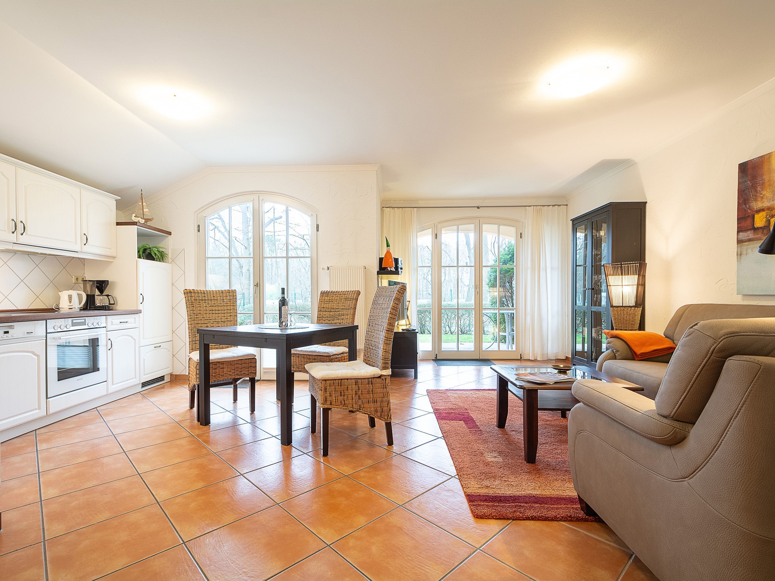 A spacious living area with a dining table, chairs, a sofa, and a kitchen with white cabinets and a tiled floor.