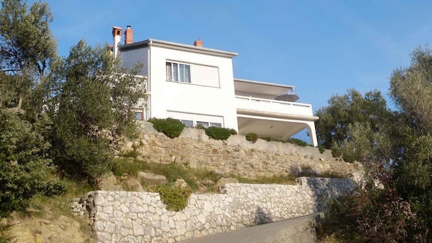 A modern two-story house with a stone retaining wall and lush greenery.