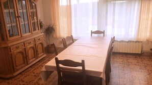 A dining room with a long table, chairs, a wooden cabinet, and a potted plant.