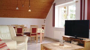 Un salon confortable avec un canapé, des fauteuils, un téléviseur et une table à manger.