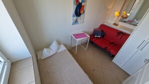 Pieni huone, jossa on sänky, pöytä, punainen sohva, jossa on kiinalaisia kirjoitusmerkkejä, seinällä oleva taulu ja vaatekaappi.