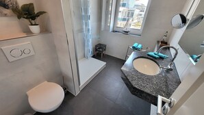 Moderni kylpyhuone, jossa on wc, pesuallas, suihku ja pieni pöytä, jonka päällä on pyyhkeitä.