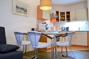 Et moderne køkken med hvide skabe, en central ø og en hængende lampe. Der er to barstole og en sort sofa i spiseområdet.