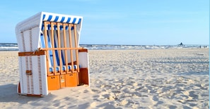 A beach chair with a striped cover and a woven backrest, positioned on a sandy beach with the ocean in the background. - House Sonnenhof Bansin - Apartment Sonnenhof 32 (Heringsdorf)