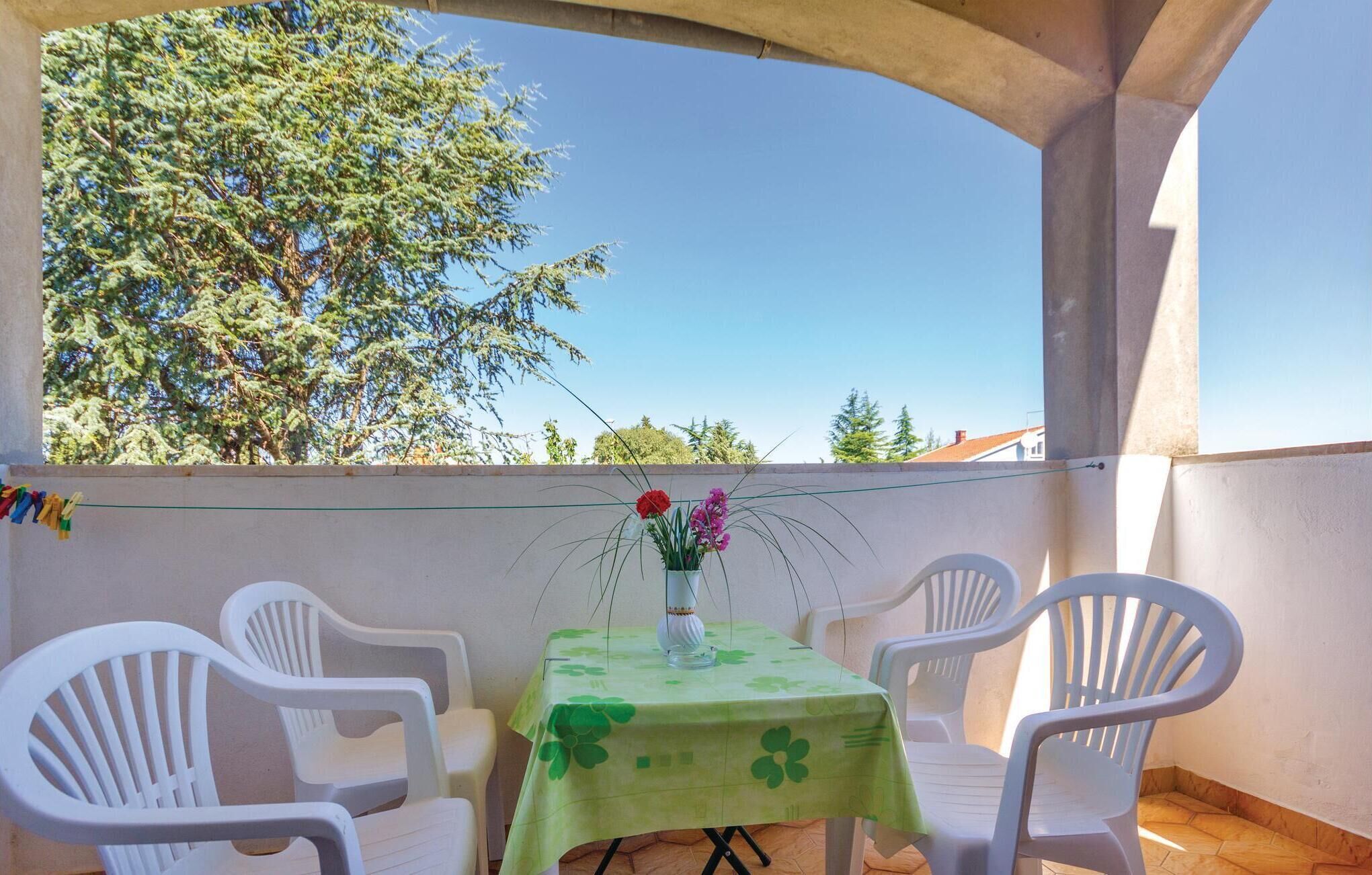 A balcony with a table and chairs, a vase with flowers, and a view of trees and buildings.