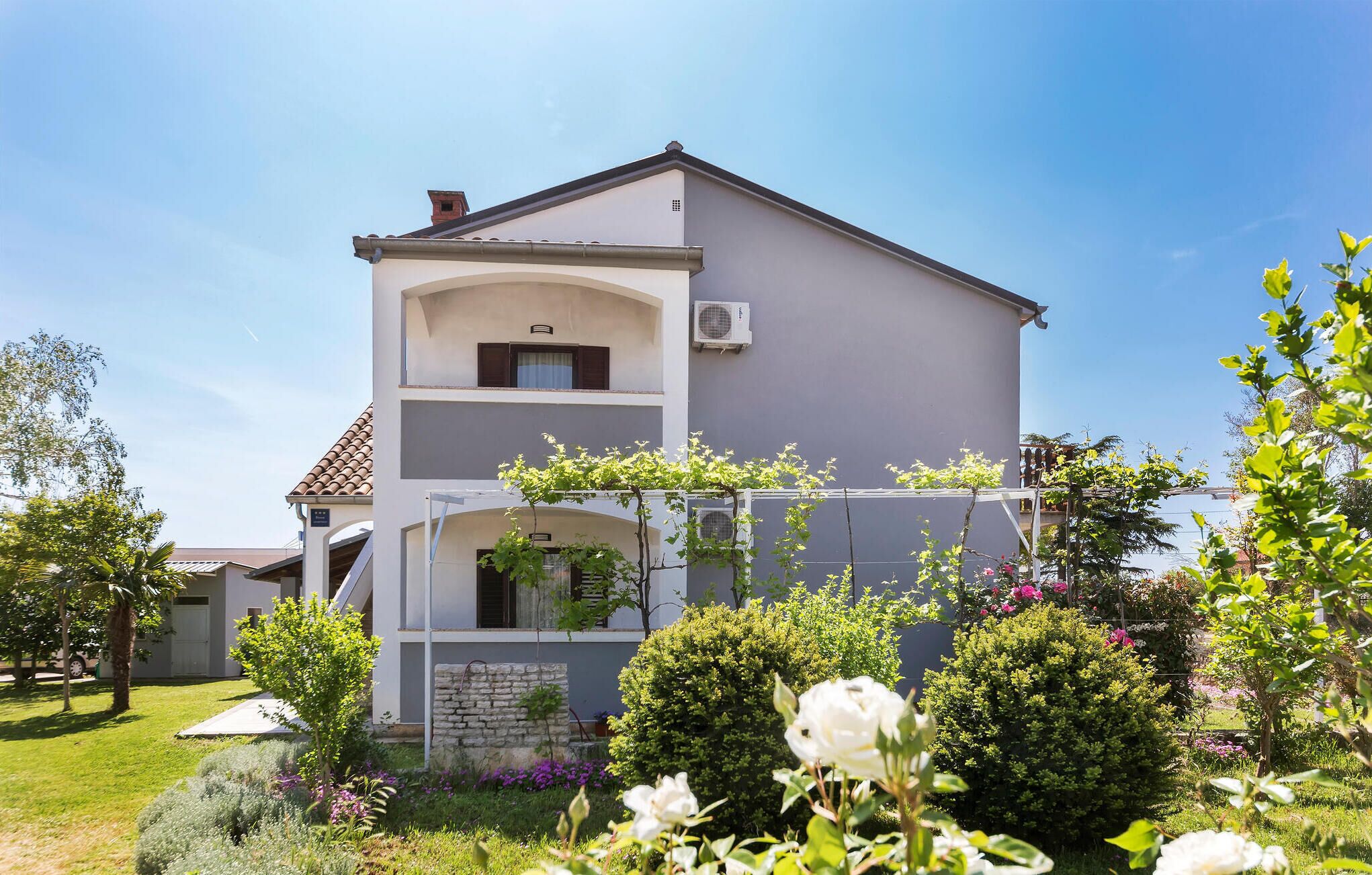 Ein zweistöckiges Gebäude mit einem Balkon, umgeben von gepflegten Gärten und blühenden Pflanzen.