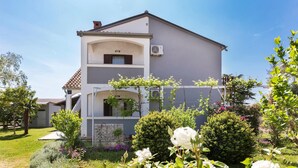 Un bâtiment à deux étages doté d’un balcon, entouré de jardins bien entretenus et de plantes en fleurs.