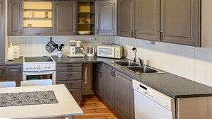 A compact kitchen with grey cabinets, a white countertop, a built-in oven, a microwave, a coffee maker, and a dishwasher.