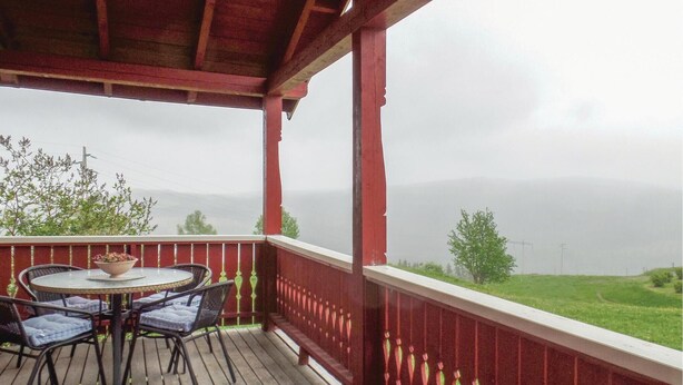 A covered outdoor area with a table and chairs, overlooking a green landscape and distant hills.