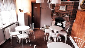 Un espace intérieur accueillant avec des tables rondes et des chaises en métal blanc, une cheminée en briques et une porte portant l'inscription « PRIVAT ».