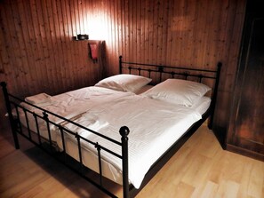 Ein Einzelbett mit Metallgestell in einem Zimmer mit Holzwänden und Holzboden.